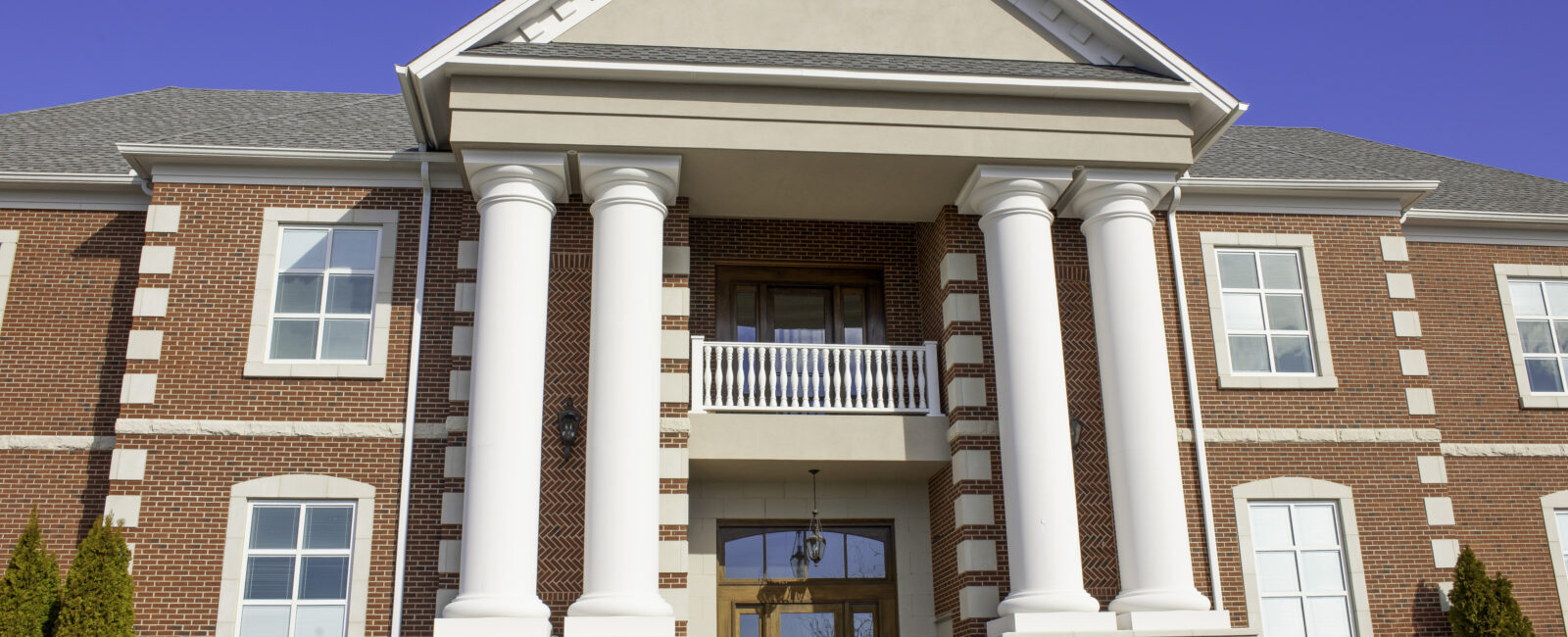 Two-story red brick building with large white columns, a peaked roof, and symmetrical windows, symbolizing stability—just as understanding what the Revised CBLR Rule means for growing community banks ensures a strong foundation on a clear day.