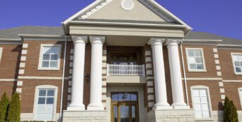 Two-story red brick building with large white columns, a peaked roof, and symmetrical windows, symbolizing stability—just as understanding what the Revised CBLR Rule means for growing community banks ensures a strong foundation on a clear day.