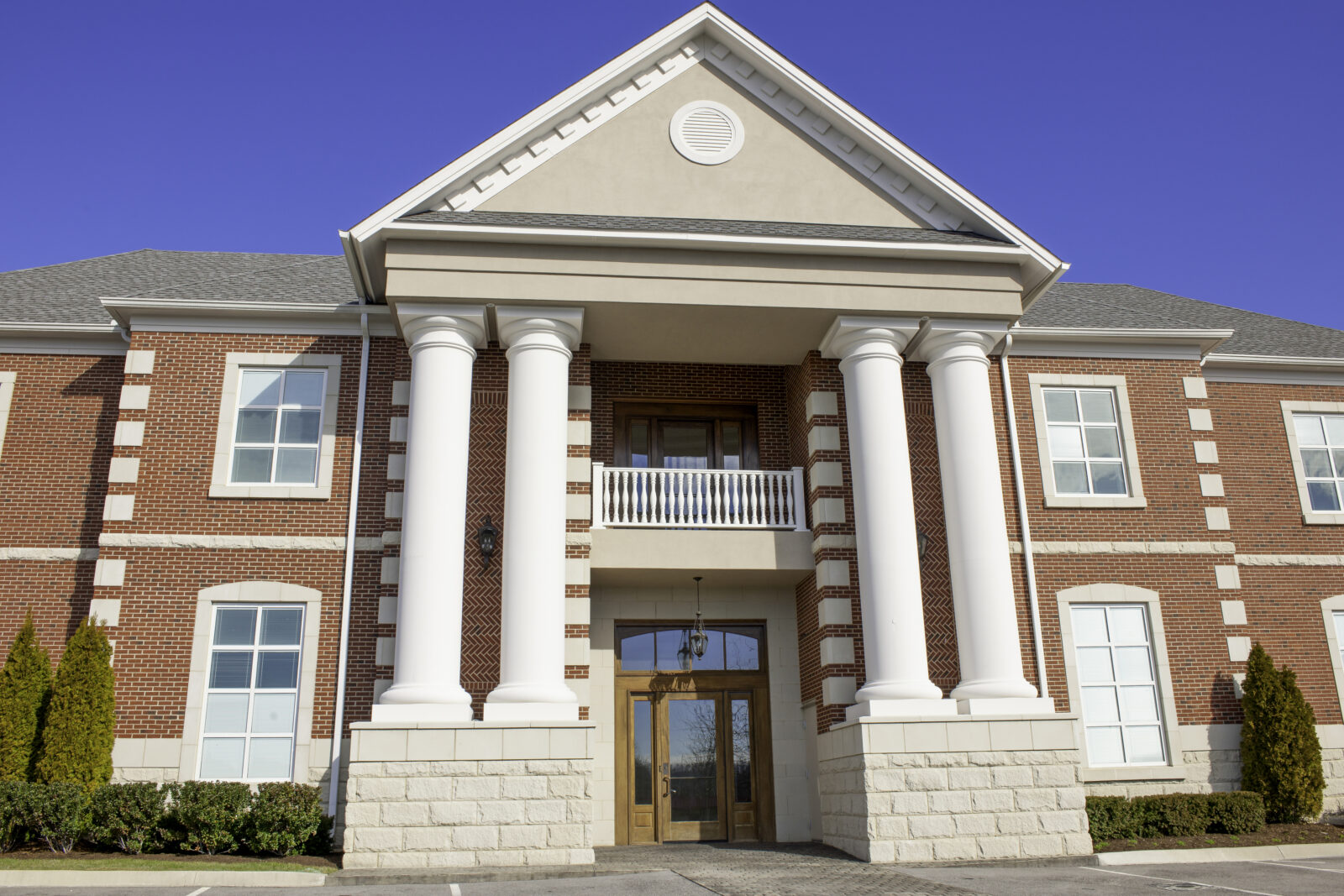 Two-story red brick building with large white columns, a peaked roof, and symmetrical windows, symbolizing stability—just as understanding what the Revised CBLR Rule means for growing community banks ensures a strong foundation on a clear day.
