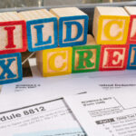 Colorful blocks spell "Child Care Tax Credit" above 1040 tax forms and IRS instructions, representing financial support for child care expenses through tax credits.