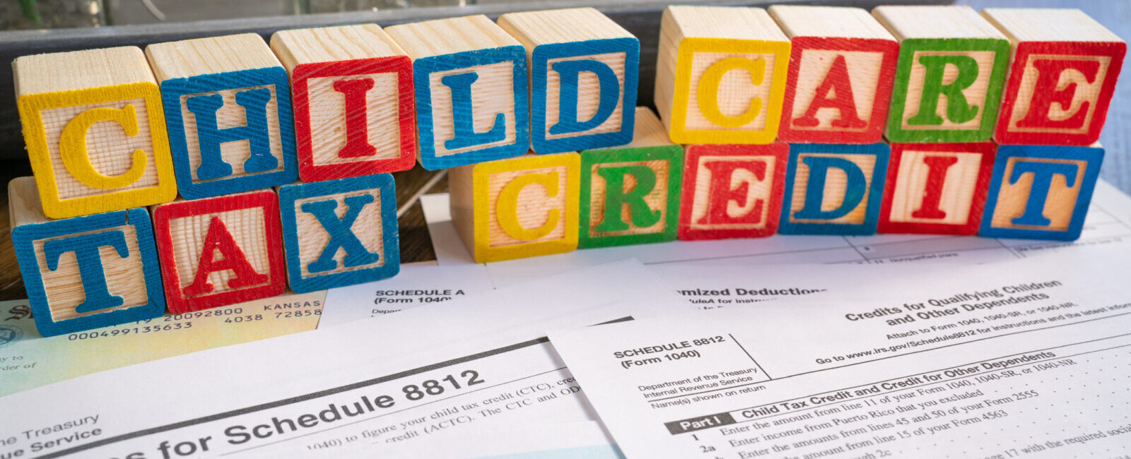 Colorful blocks spell "Child Care Tax Credit" above 1040 tax forms and IRS instructions, representing financial support for child care expenses through tax credits.