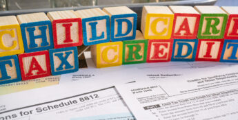 Colorful blocks spell "Child Care Tax Credit" above 1040 tax forms and IRS instructions, representing financial support for child care expenses through tax credits.