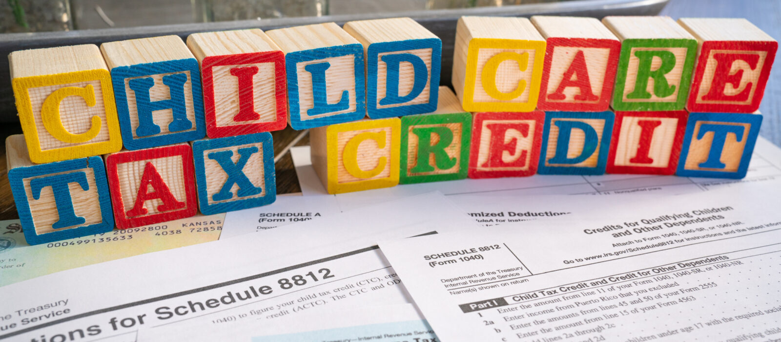 Colorful blocks spell "Child Care Tax Credit" above 1040 tax forms and IRS instructions, representing financial support for child care expenses through tax credits.