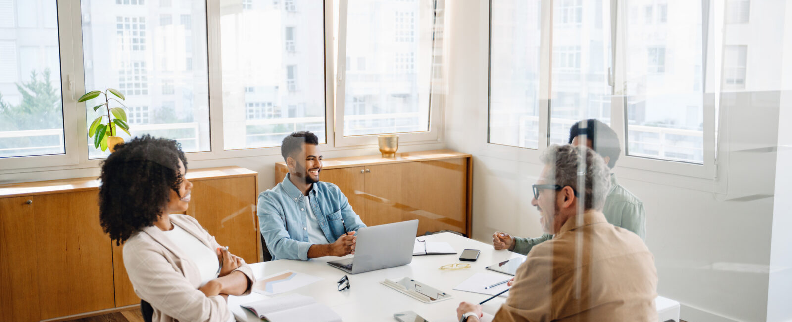 Four people sit around a table in a modern office, engaged in a meeting with laptops, notebooks, and paperwork visible—a setting where peer groups are leadership think tanks, fostering collaboration and innovative problem-solving.