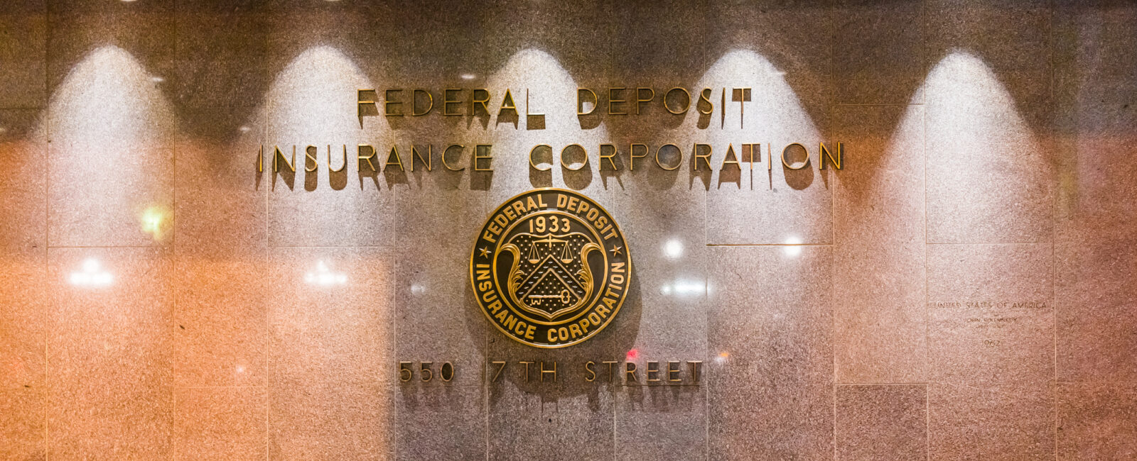 Lobby wall with "Federal Deposit Insurance Corporation" and seal, along with the address "550 17th Street" inscribed in gold lettering, highlights recent updates as the FDIC Signage Deadline Extended to 2027.
