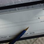A blank check in a checkbook with a pen resting on it, ready to be written, showing check number 1456 and account details at the bottom—a subtle reminder of how easily such financial tools can contribute to check fraud losses if not handled securely.