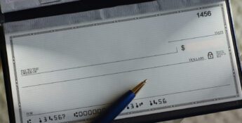 A blank check in a checkbook with a pen resting on it, ready to be written, showing check number 1456 and account details at the bottom—a subtle reminder of how easily such financial tools can contribute to check fraud losses if not handled securely.