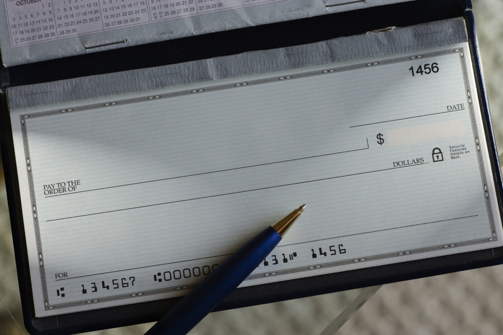 A blank check in a checkbook with a pen resting on it, ready to be written, showing check number 1456 and account details at the bottom—a subtle reminder of how easily such financial tools can contribute to check fraud losses if not handled securely.
