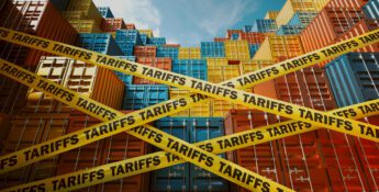 Stacks of colorful shipping containers are blocked by yellow tape labeled “TARIFFS,” symbolizing trade barriers. Blue sky and scattered clouds are visible above the containers.