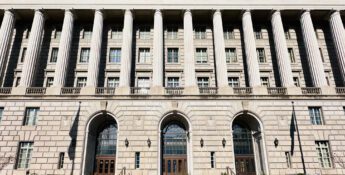 Large neoclassical government building with tall columns, arched doorways, numerous windows, and several small potted plants arranged in a row in front—an imposing structure that could easily serve as the backdrop for important announcements, such as when the IRS increases standard mileage rates.