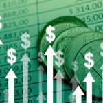 Coins on top of a financial spreadsheet with upward-pointing arrows and dollar signs, symbolizing financial growth or profit increase.