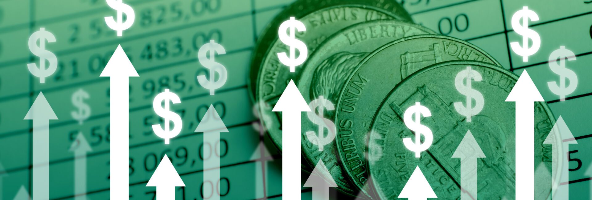 Coins on top of a financial spreadsheet with upward-pointing arrows and dollar signs, symbolizing financial growth or profit increase.