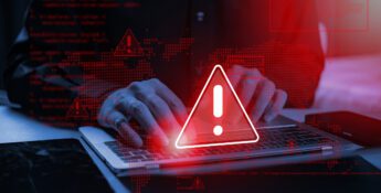 Hands typing on a laptop with a digital overlay of red warning icons and computer code.