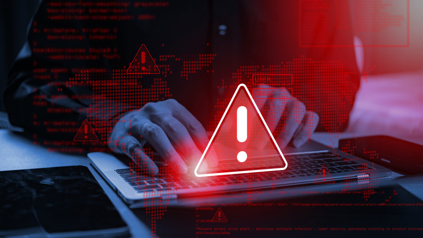 Hands typing on a laptop with a digital overlay of red warning icons and computer code.