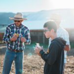 A young boy and two men in hats eating farm meals on a ranch.
